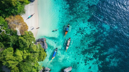 Aerial view of crystal-clear waters, a white beach, and long-tail boats on a tropical island in Southern Thailand.