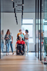 Fototapeta premium A diverse group of young business people walking a corridor in the glass-enclosed office of a modern startup, including a person in a wheelchair and a woman wearing a hijab