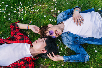 Latino and Chinese gay couple lying in a flower-filled park, showing love and pride with LGBT...