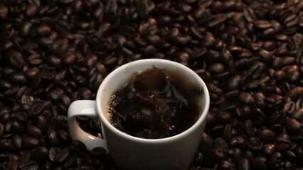 Close up of coffee bean drop in to hot espresso with pile of coffee seed. Macro of freshly roasted...