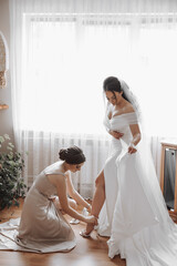 A woman in a wedding dress. A friend helps the bride put on her shoes. Wedding dress. Preparation...