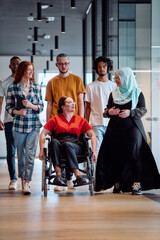 A diverse group of young business people walking a corridor in the glass-enclosed office of a...