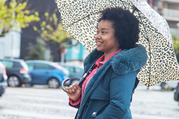 afro woman on the street walking with umbrella in the rain