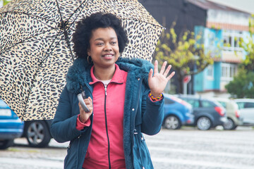 afro woman on the street walking with umbrella and waving