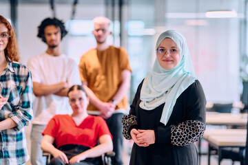 A diverse group of young business people walking a corridor in the glass-enclosed office of a modern startup, including a person in a wheelchair and a woman wearing a hijab