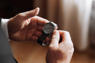 A man is holding a watch in his hand. The watch is black and silver. The man is wearing a suit