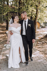 Fototapeta premium A bride and groom are walking down a path, the bride is holding a bouquet and the groom is wearing a tie