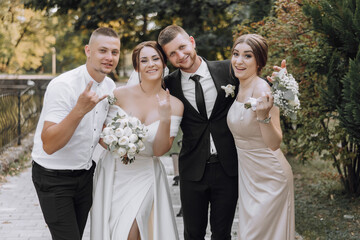 A bride and groom are posing for a photo with their friends. The bride is wearing a white dress and...