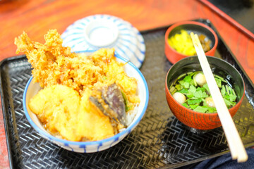 Donburi, Japanese food, mixed deep fried seafood and vegetables on rice in a bowl, with a cup of soup in black wooden tray, isolated on wooden table, closed up, top view, flat lay