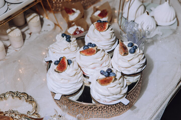 A table with a variety of desserts, including cupcakes with blueberries and whipped cream. The desserts are arranged on a gold tray, and there are several other desserts on the table as well