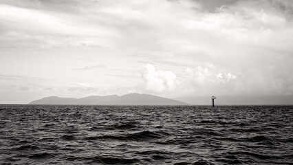 moody ocean seascape, monochrome black and white, choppy rough water, clouds, island with sea spray, dramatic dark cinematic atmospheric