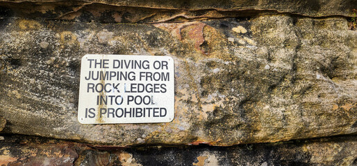 A sign about The diving or jumping from rock ledges into pool is prohibited