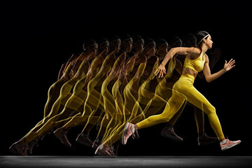 Dynamic image of young woman in yellow sportswear in motion, training, running against black...