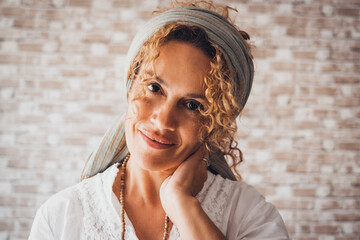 Happy curly woman smiles looking at the camera. Frontal portrait of a middle-aged lady with bricks indoor home background. One cute midage female people smiling and looking at you. Cheerful lady