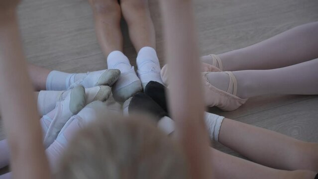 Top view of the legs of little ballerinas sitting on the floor in a circle. 