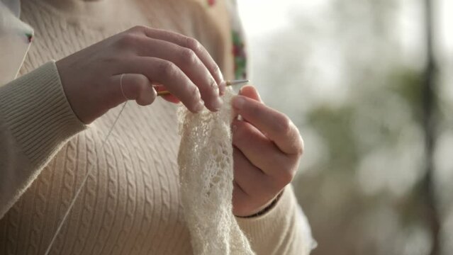 Close up of cashmere crochet work from sheep's wool. Hands of an attractive caucasian woman in casual clothes knitting a wool product with crochet.