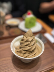 A Japanese milk chocolate soft serve ice cream in a bowl in the foreground and a slice of green tea cake in the background