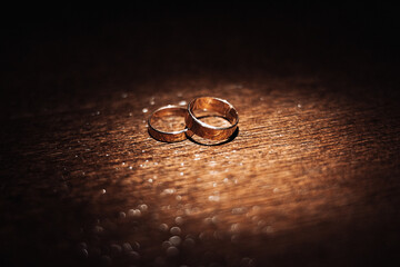 Two gold wedding rings are placed on a wooden surface. The rings are positioned close to each...