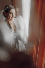 A woman in a white gown is looking out a window. The image has a soft, dreamy quality to it, with...