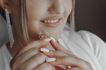 A woman is holding a ring in her hand, and she is smiling. The ring is a diamond ring, and it is a beautiful piece of jewelry. The woman's smile suggests that she is happy and proud of the ring - Powered by Adobe