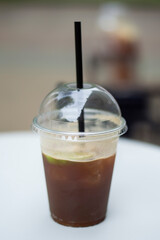 Iced coffee in plastic cup with black straw on table