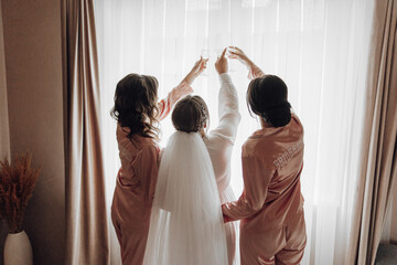 Three women in pink gowns are celebrating a wedding. One of them is holding a glass of wine