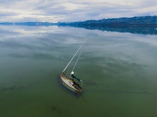 Sunken abandoned yatch and forest mountains with snow. Tahoe Keys, South Lake Tahoe, California,...