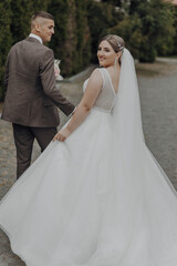 Naklejka premium A bride and groom are walking down a path in a wedding dress and suit. The bride is holding a bouquet and the groom is holding her hand
