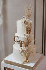 Three-tier wedding cake with gold trim and white icing, decorated with dried flowers. Decorative cake