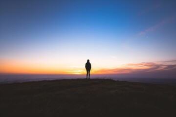 Step into the serene silhouette of a lone figure standing on a hilltop, watching as the sun sinks below the horizon and casts long, Generative AI