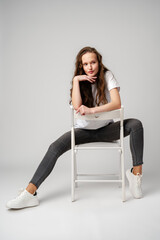 Fototapeta premium Curly girl model posing on a chair against gray background