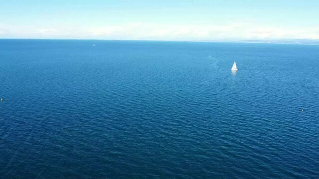 Aerial push from shore to sea with sailboat in background on blue sea.