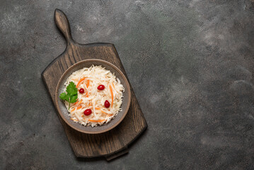 Sauerkraut with cranberries and carrots in a bowl on a wooden cutting board, dark grunge background. Top view, flat lay, copy space