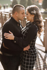 A man and woman are hugging each other on a bridge. The man is wearing a black shirt and the woman is wearing a black dress with a black and white pattern