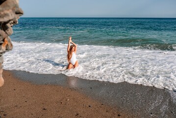 Happy woman in bikini sits on the sea beach. Tanned girl sunbathing on a beautiful shore. Summer...