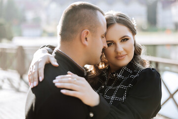 A man and woman are hugging each other on a bridge. The man is wearing a ring on his left hand