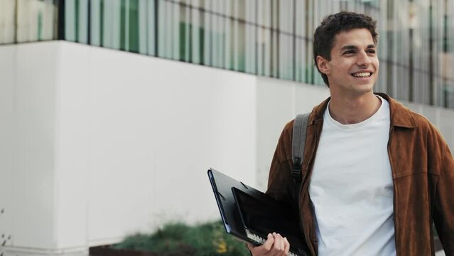 Carefree Young man walking in the university campus. Inspired phd student and smiling in the city