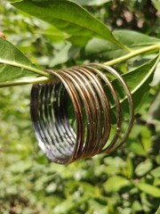 A set of metallic golden color bangles hanging on wooden stick with green leafy background, round golden brown bangles jewllery photography