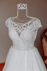 A white dress with a lot of sparkles on it. The dress is hanging on a white metal stand