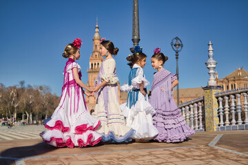 Four girls dancing flamenco, talking to each other, in typical flamenco costumes on a bridge in a beautiful square in Seville. Dance concept, flamenco, typical Spanish, Seville, Spain.