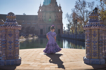 A girl dancing flamenco, in typical flamenco dress, with her back turned, receiving the sun's rays, next to a lake in a beautiful square in Seville. Concept dance, flamenco, typical Spanish, Spain.