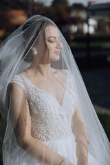 A woman wearing a veil and a white dress. She is looking at the camera. The veil is white and has a...