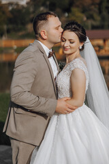 A bride and groom are kissing each other's cheeks. The bride is wearing a white dress and the groom...