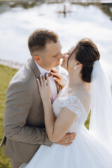 A bride and groom are embracing each other in a grassy field. The bride is wearing a white dress...