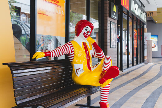 BANGKOK, Thailand - April 27, 2024 : ronald-mcdonald sitting on bench in front of  McDonald's restaurant
