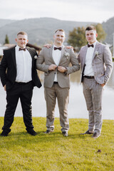 Three men in suits pose for a photo by a body of water. Scene is formal and relaxed, as the men are...