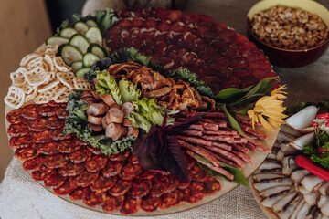 A large platter of assorted meats and vegetables is displayed on a table. The platter is filled with a variety of meats, including sausage, ham, and salami, as well as vegetables such as lettuce