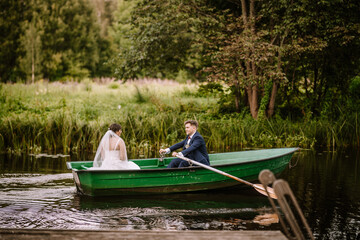 Valmiera, Latvia - August 19, 2023 -  a bride and groom in a green rowboat on a river, with lush...