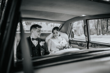 Valmiera, Latvia - August 19, 2023 - A bride and groom sit in the back of a vintage car, smiling...