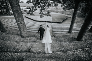 Valmiera, Latvia - August 19, 2023 - A bride and groom walk down steps toward an outdoor...